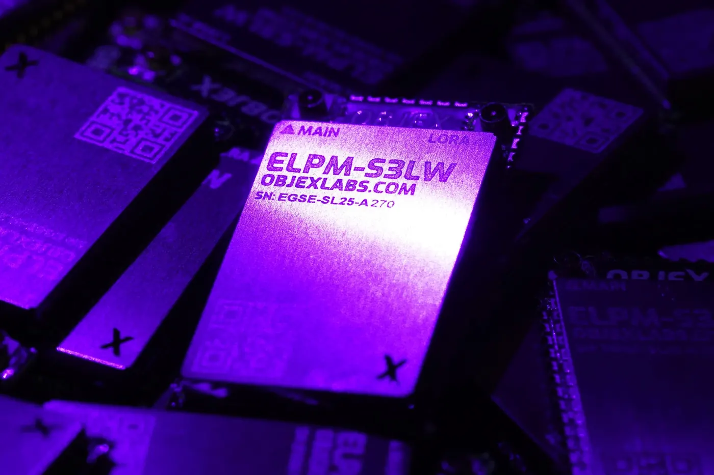 OBJEX ELPM-S3LW modules under violet light, the front module's shield reads ELPM-S3LW, objexlabs.com