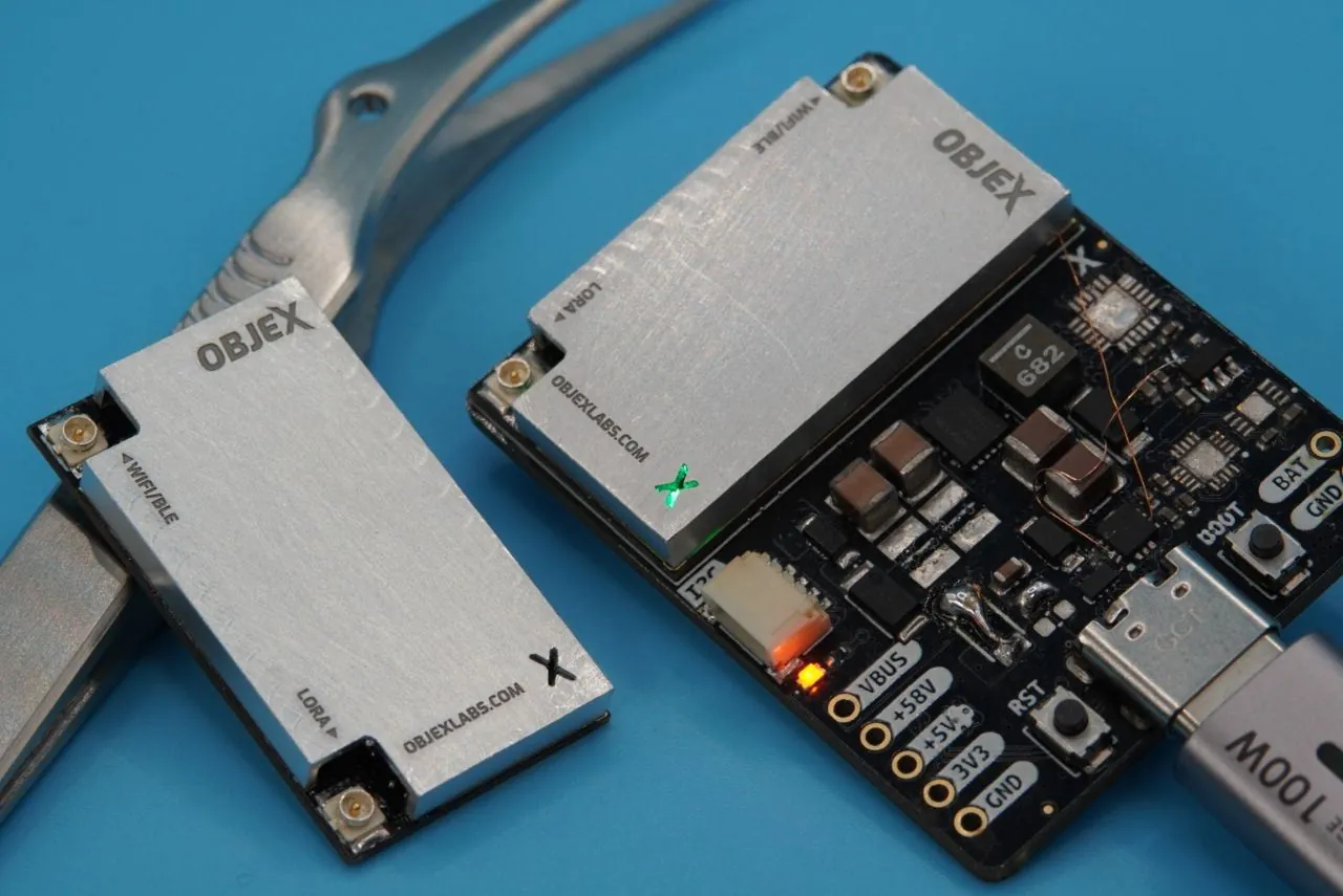 Two ELPM-S3LW modules on a blue mat, one with its metal shield on, one showing the bare PCB, beside a metal tool