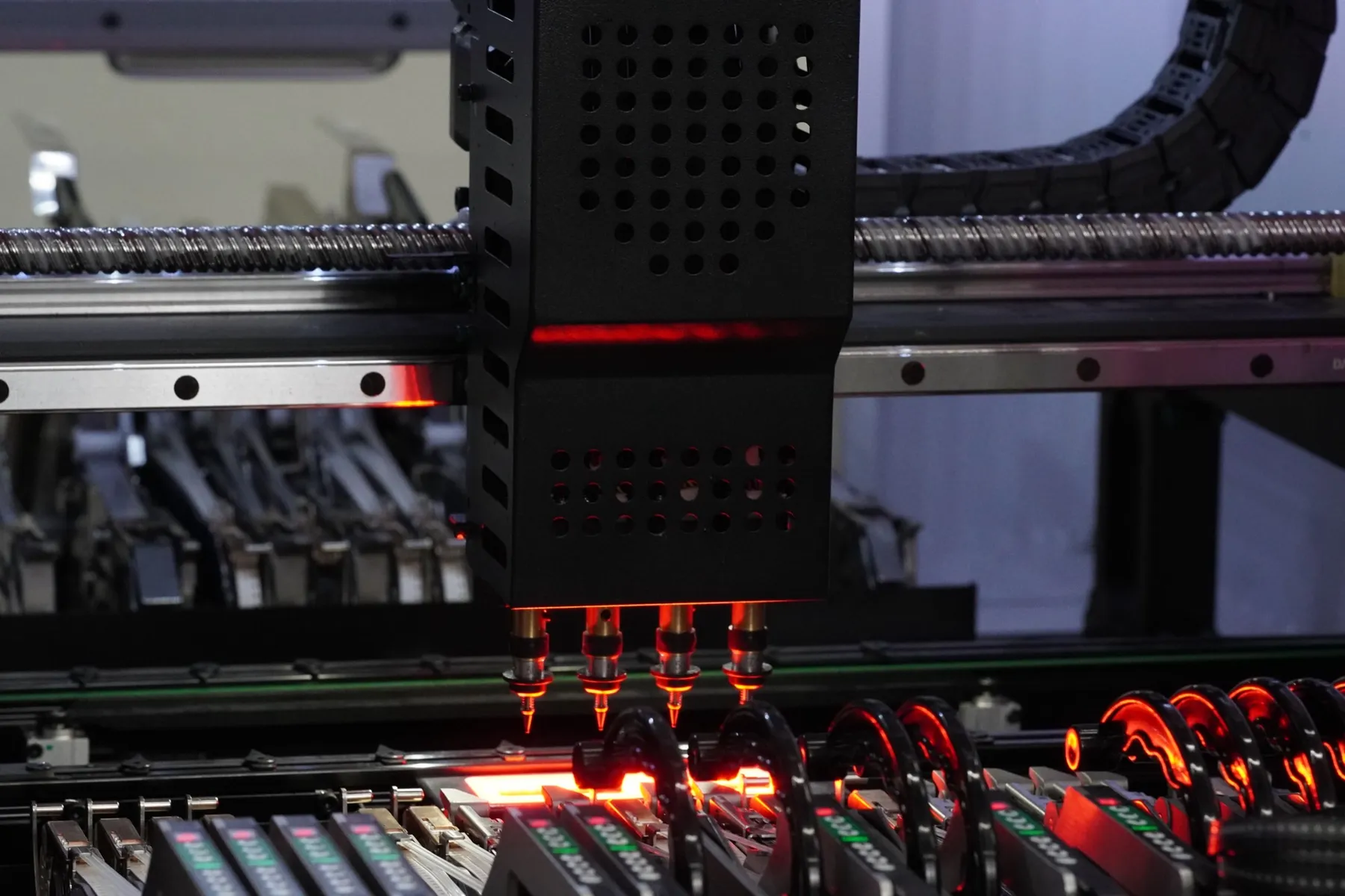 Pick-and-place head with four nozzles over the component feeders, lit red, on the OBJEX assembly line